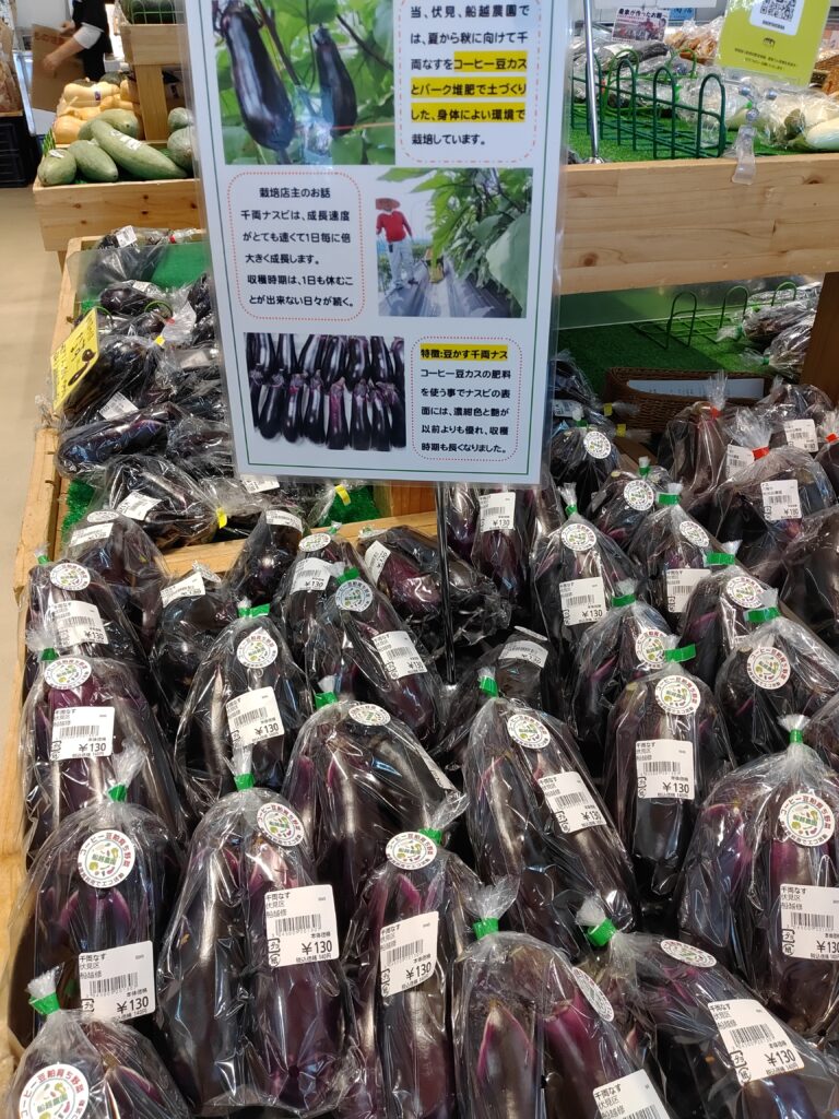 じねんと市場で販売されている舩越農園の千両なす。コーヒーかすとバーク堆肥を活用した栽培方法を紹介するポップと一緒に並んでいる様子。