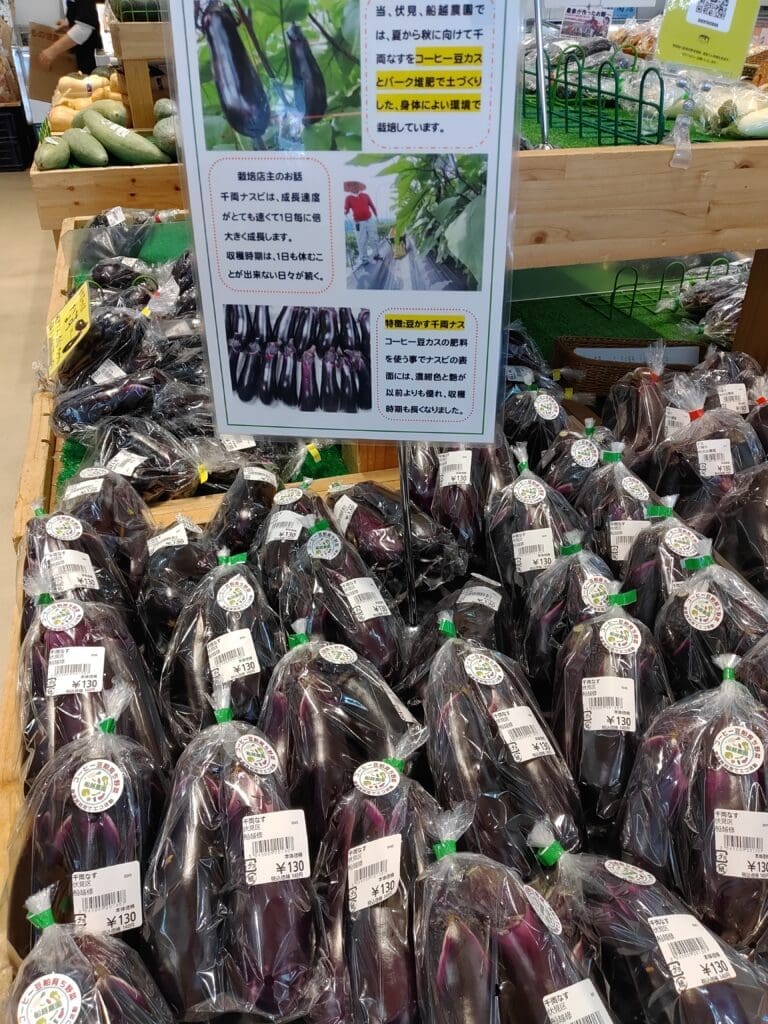 じねんと市場で販売されている舩越農園の千両なす。コーヒーかすとバーク堆肥を活用した栽培方法を紹介するポップと一緒に並んでいる様子。