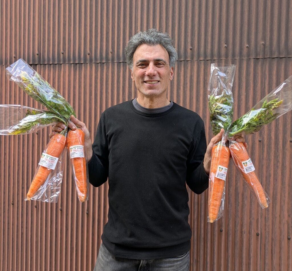 コーヒーかすの堆肥で育った葉付き人参を両手に持つ様子（mame-ecoラベル付き）