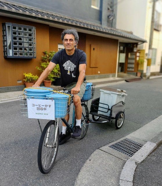 西陣の静かな通りを、青いコーヒーかす回収バケツを載せたマウンテンバイクとトレーラーで走るmame-eco(マメエコ)のGary。